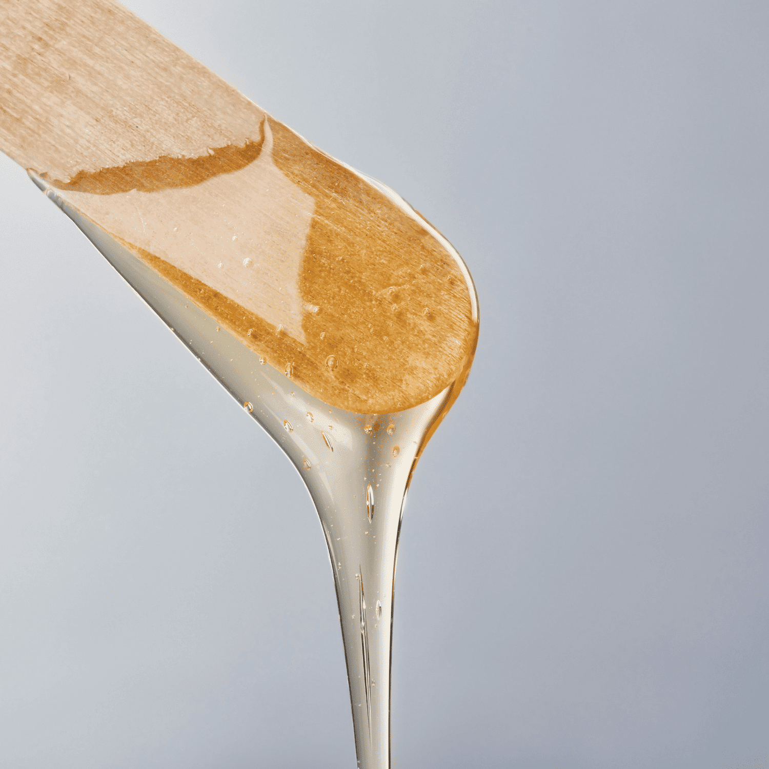 Wooden spatula dripping with honey against a light grey background.