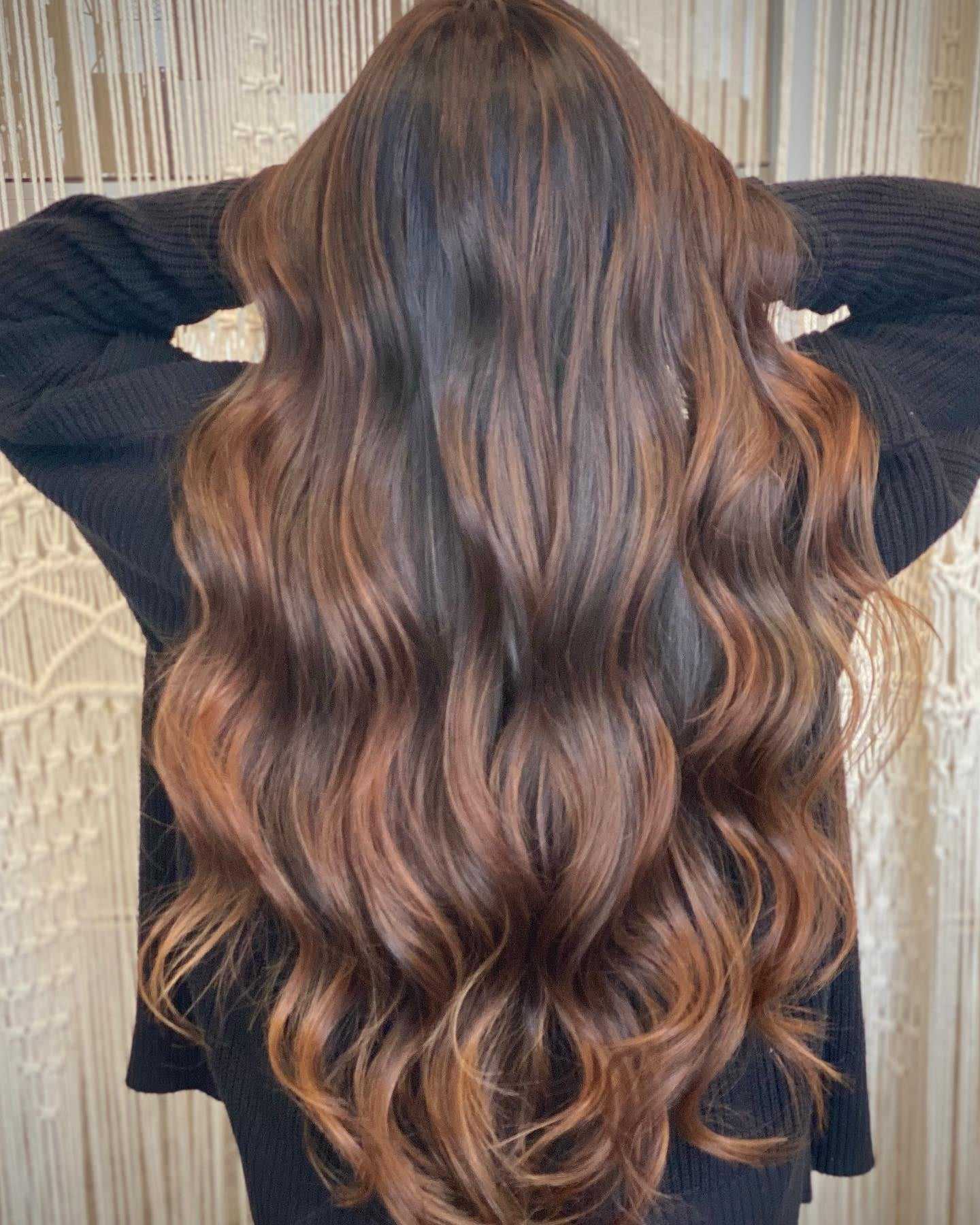 Woman with long wavy brown hair with caramel highlights.