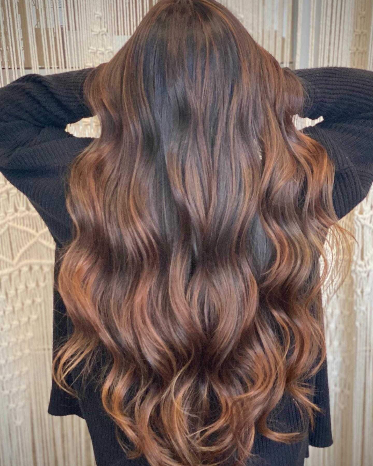 Woman with long wavy brown hair with caramel highlights.