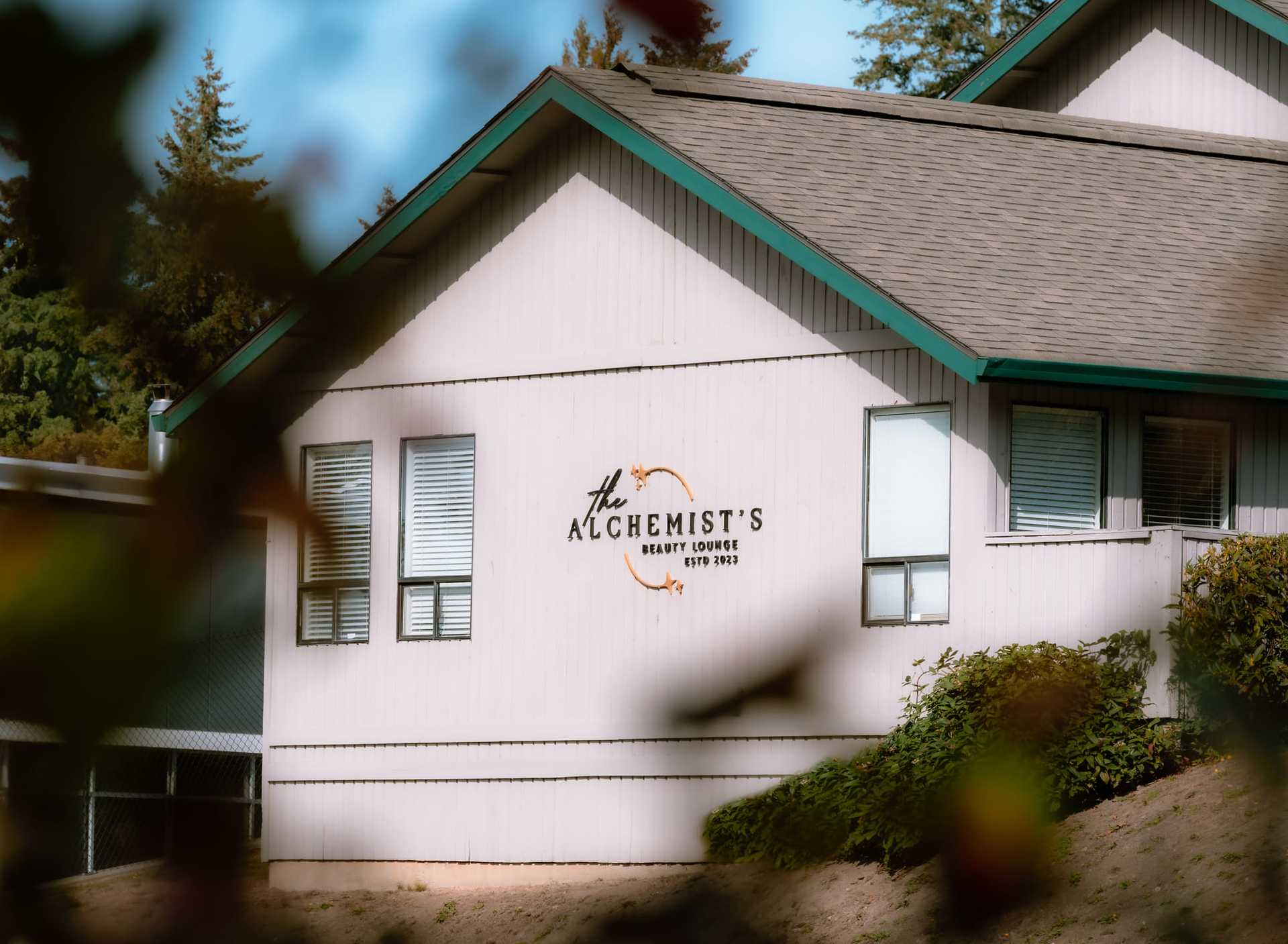 A cozy building with "The Alchemist's Heart Lodge, estd. 1923" sign, surrounded by trees.