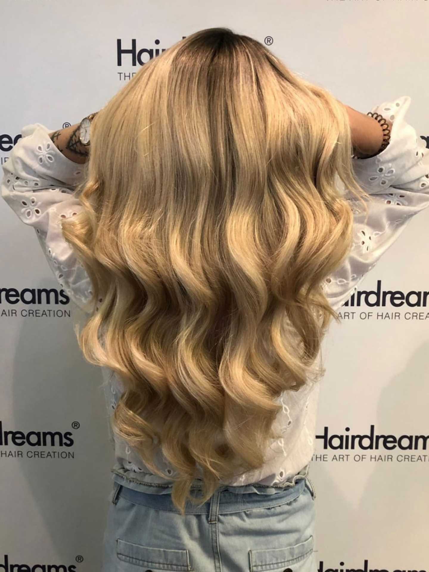 Woman showcasing her long, wavy blonde hair extensions from the back.